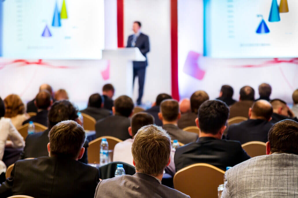 Sprecher auf einem Podium in einer Konferenzhalle aus dem Hintergrund fotografiert
